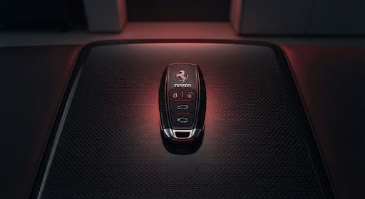 Modern sports car key resting on a carbon-fiber surface with red backlighting